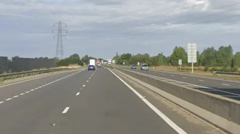 Google Maps A dual carriageway has a few cars driving on either side of the road. There is a barrier which runs in between the roads.