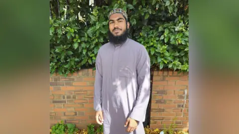 Faizan Rafik is pictured wearing a long grey shirt and long beard