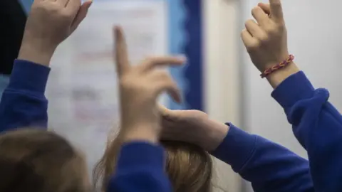 PA média Obecný obraz neidentifikovaných žáků základních škol, který drží ruce vzhůru, zatímco nosí modré mikiny.