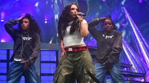 Getty Images Jade Thirlwall singing onstage - she is wearing a white top with grey/green trousers, and has long dark hair past her shoulders. Two backing dancers are behind her. both in blue jeans and grey tops.