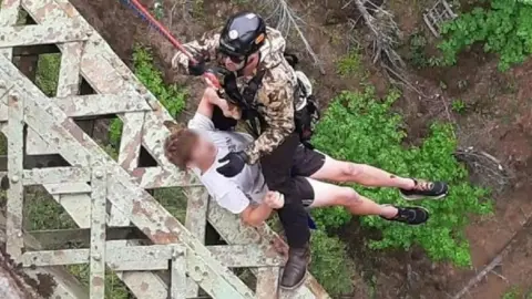 A rescuer using a harness pulls a teenager to safety