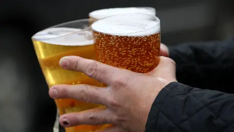 Three full drink glasses being held in the hands of someone wearing black. The dark background is blurred.