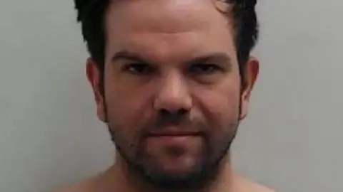 Police Scotland Jamie has short dark hair. He has a dark short beard.