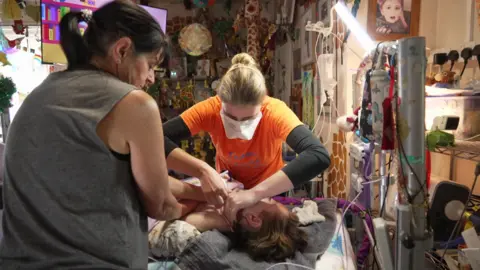 Jenny Dunning/BBC Samantha and one of Lewis' nurses cleaning his neck for his tracheostomy tape change. 