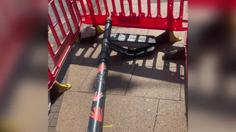A green sign post is pictured lying on the ground with orange barriers surrounding it.