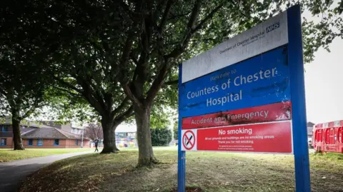 A blue sign in front of a footpath reads 'Countess of Chester Hospital' 