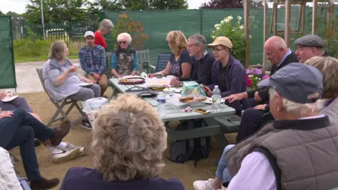 Volunteers sit around a large picnic table eating cakes