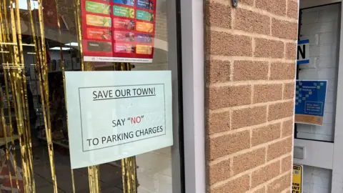 A shop window with a a poster on it that says save our town, say no to parking charges