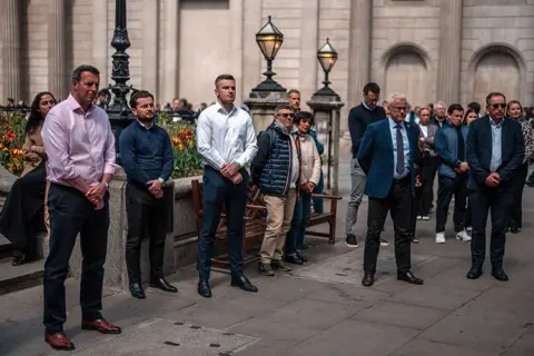 Carl Court/Getty Images People stand outside the Bank of England as they observe a two minute silence to mark the 80th anniversary of VE Day on May 8, 2025 in London, England.