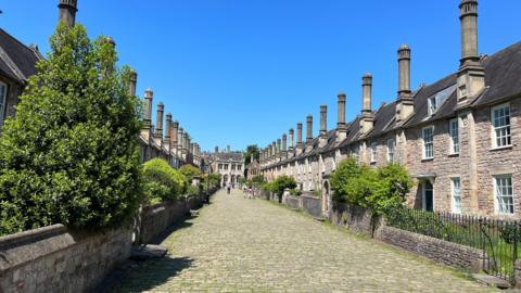 A cobbled street of period terraced houses with chimneys