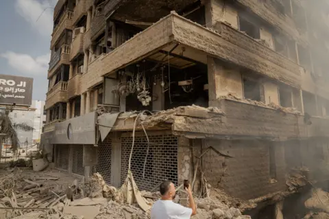 Joel Gunter/BBC Charred lighting hangs in the bombed out shop belonging to Shakeeb Saleh, in Dahieh. 