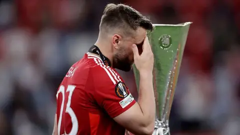 Luke Shaw walks past the Europa League trophy