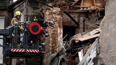 PA Media Emergency services use a raised platform to access the ruined flat that exploded in Alloa