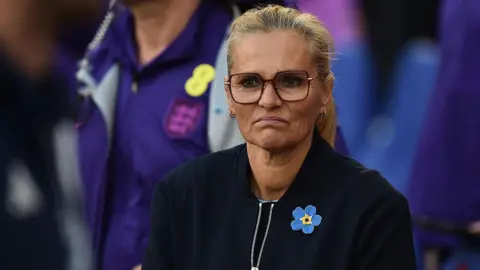 A frowning Sarina Wiegman in dark top and yellow and blue broach