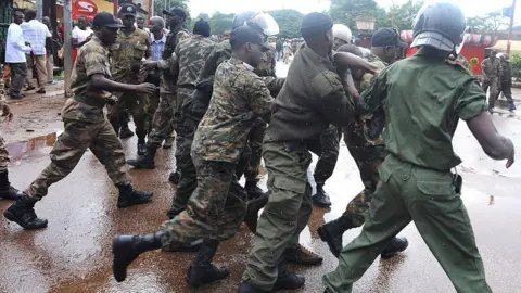 AFP via Getty Images Police standing in a line - with their backs to the camera - pushing against protesters 