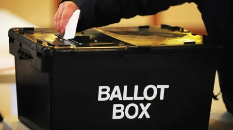 A voter casts their vote in a black ballot box