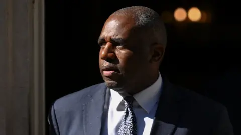 David Lammy, wearing a white shirt and blue tie, emerges from Downing Street