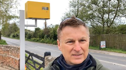 Guy Hayward standing with his fake speed camera on his farm
