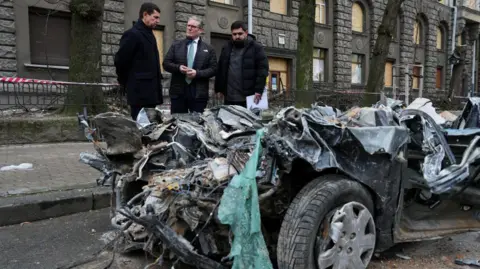 ウクライナ当局者に先導され、道路沿いで破損した車両を点検する首相