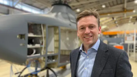 Nigel Colman, managing director of Leonardo Helicopters UK, stands in front of the body of one of the new helicopters inside a hangar.