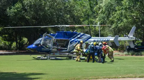 South Walton Fire District A crowd of people taking someone towards a rescue helicopter which has landed on grass