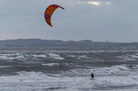 Iolaire/BBC Weather Watchers A kite surfer rides choppy waves off the beach at Dornoch in the Highlands.