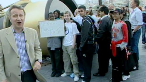 Presenter wearing beige jacket stands beside a crowd of young people at the tunnel-like Telectroscope.