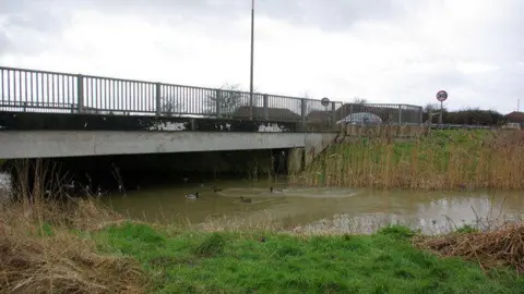 Robin Webster/Geograph The Aldingbourne Rife a stream which runs through Bognor. There is a bridge for traffic over the top of it and there are ducks swimming in the stream.
