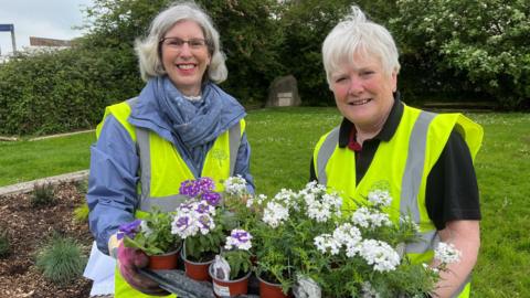 Two volunteers holding flowers for the towns' displays