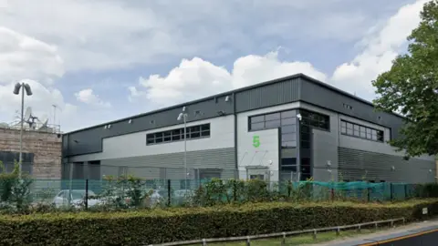 An image of a large black and grey building with a smaller light brown building on the left side covered in satellite dishes.