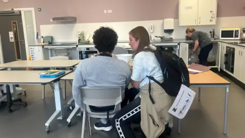 Photograph of the kitchen in the Ged Mason building at the Seashell Trust. The image shows a teacher giving one of the students a cookery lesson.