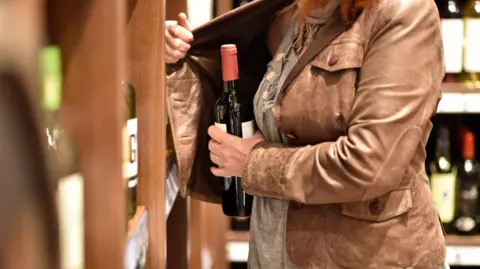 A person putting a wine bottle inside their brown leather jacket.