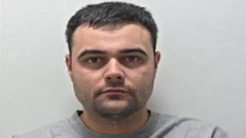 Cash McLaughlin's mugshot. He has short brown hair and stubble and is wearing a grey sweatshirt