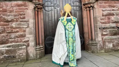 Right Reverend Patricia Hillas seen form the back standing in front of the cathedral doors, whcih are closed.