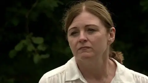 Debbie Adlam wearing a while blouse, in front of a dark background of shrubs