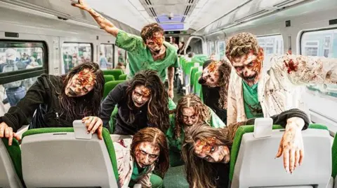 PLASTER COMMUNICATIONS Eight people dressed as zombies sat on a train