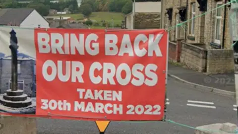 Google A red banner tied over a road that reads: Bring back out cross taken 20th March 2022