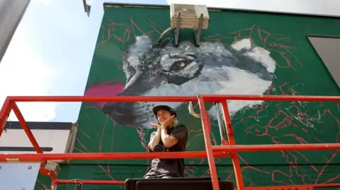 Art of Protest An artist is standing on red scaffolding with a large mural behind them