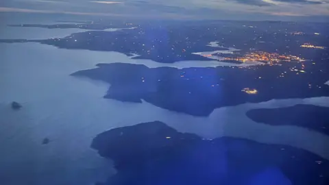 Andrew Wilson An aerial view over the east coast of Ireland taken from a plane by Andrew Wilson.  It shows a sparsely lit coastal area, a river channel and city lights in the background.