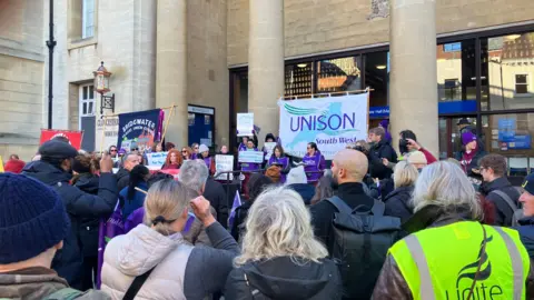 A group of protesters holding Unison signs stand outside Shire Hall in Gloucester