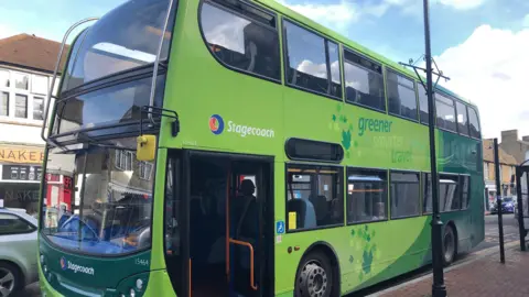 A green double-decker bus at a bus stop.