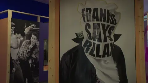 Museum of Liverpool Painting of a man with a bag that says "Franke Says Relax" over his head. In the background, a picture of Holly Johnson singing while a shirtless man in a cowboy hat dances next to him.