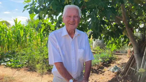 Sue Kinnear An older man in a white shirt standing in a field with very tall vegetation 
