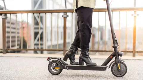 An e-scooter being ridden by someone wearing high-heel boots, in close-up
