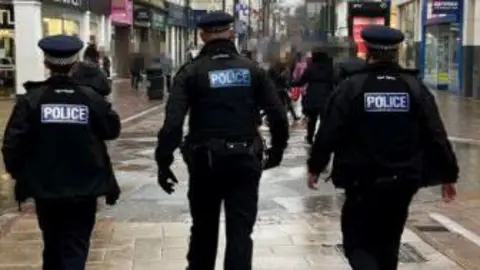 Three police officers seen from behind as the walk through Chatham town centre.