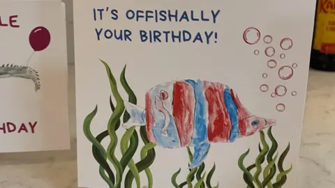 The photo shows a hand-drawn birthday card featuring a colourful fish and seaweed.