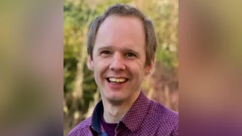 Green Party Councillor Jonathon Chilvers wearing a purple shirt and stood outside, smiling at the camera