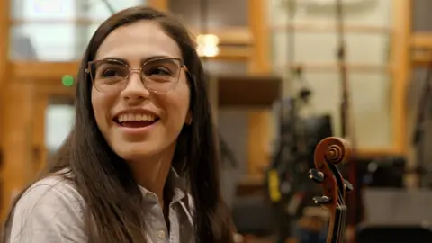 BBC Pathrycia Mendonça smiles while holding her violin