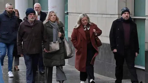 Pacemaker A group of people walking on a street. There are four men and four women. One of the men is holding hands with another woman, the rest are walking individually.