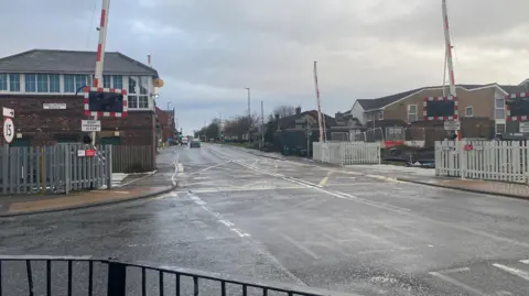 A level crossing at Bedlington with both the barriers raised. To one side construction work can be seen.